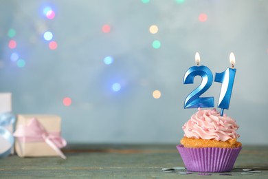 Photo of 21th birthday, coming of age party. Delicious cupcake with number shaped candles on light blue table, space for text