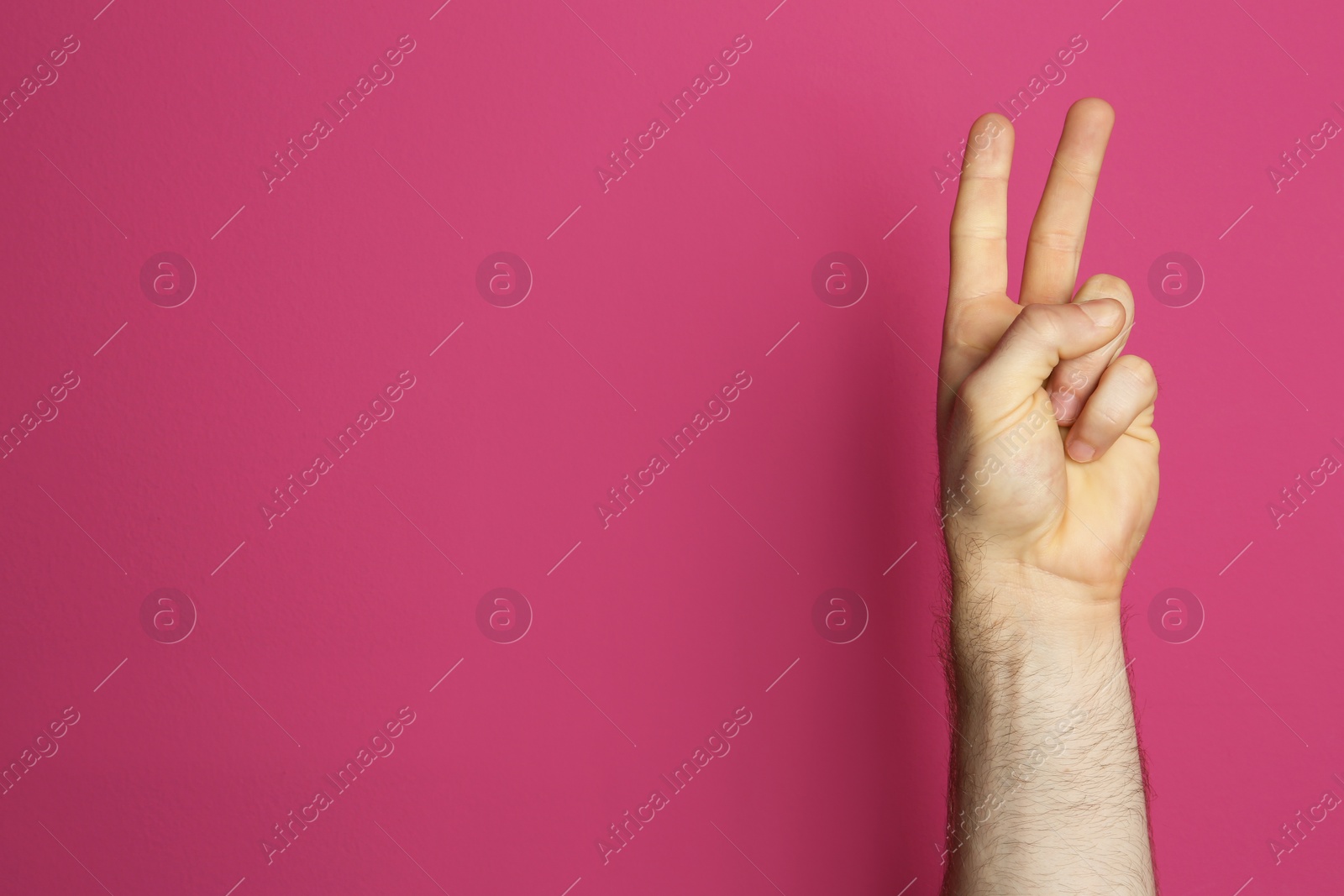 Photo of Young man showing victory gesture on color background. Space for text