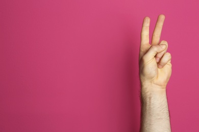 Photo of Young man showing victory gesture on color background. Space for text