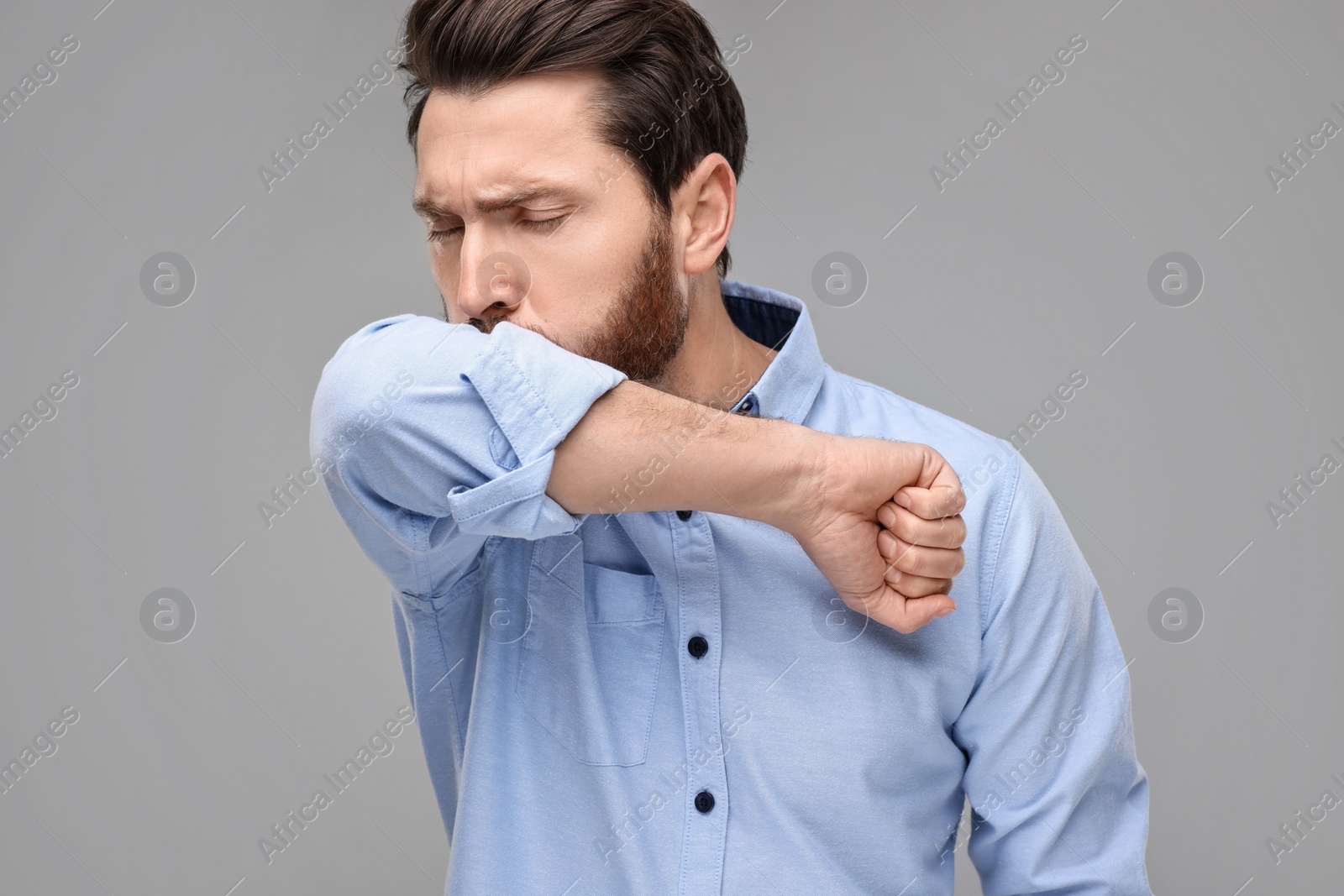 Photo of Sick man coughing into his elbow on light grey background. Cold symptoms