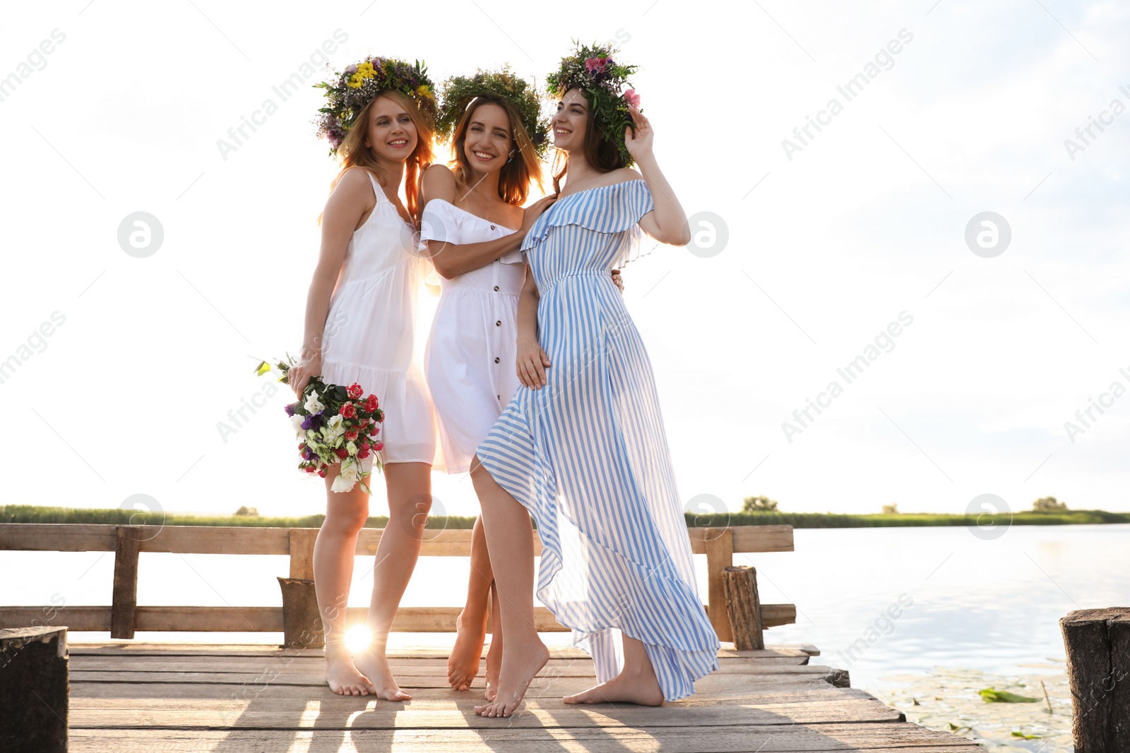 Photo of Young women wearing wreaths made of beautiful flowers on pier near river