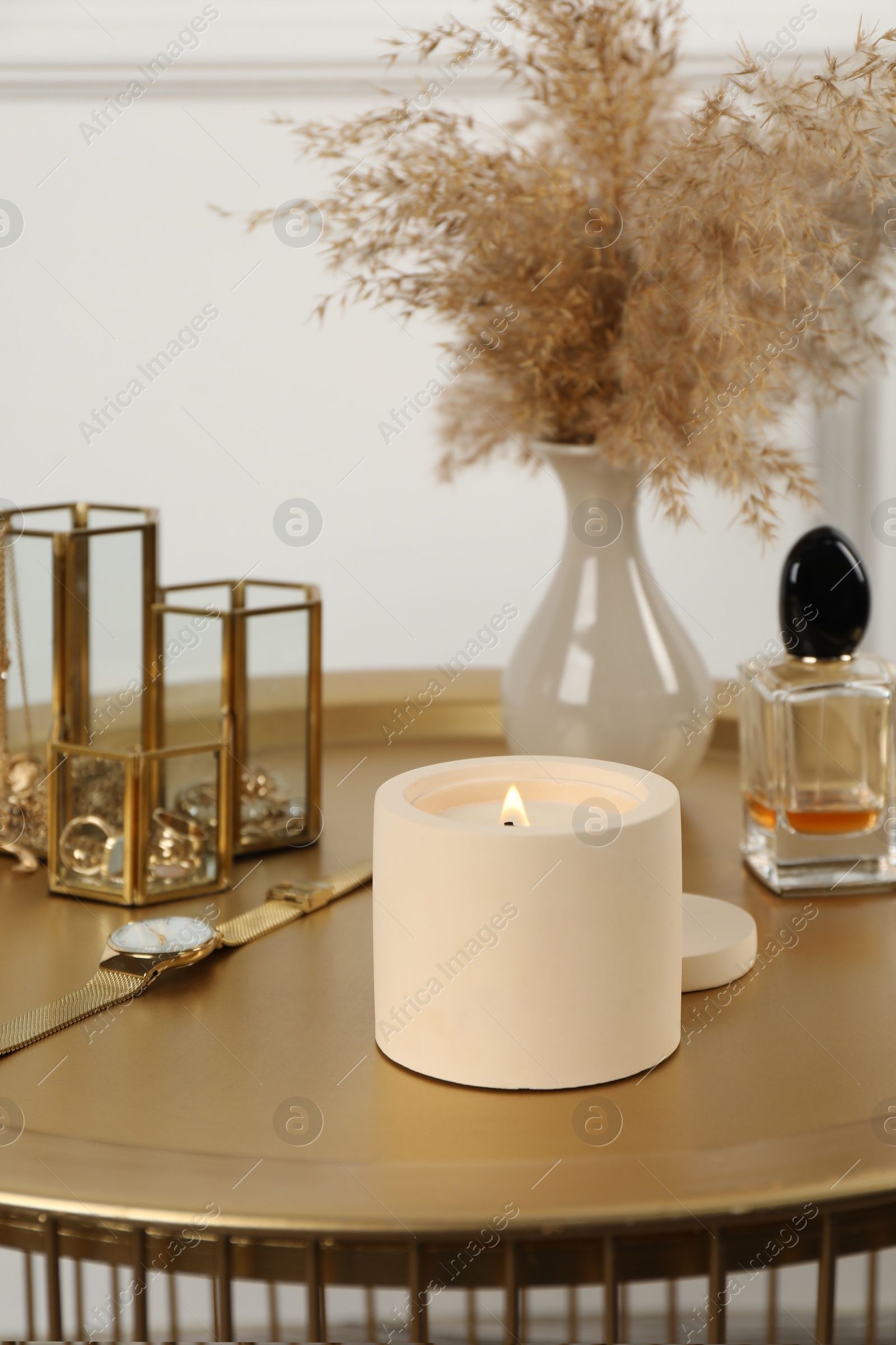 Photo of Burning soy candle, perfume and stylish accessories on table indoors