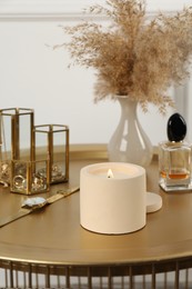 Photo of Burning soy candle, perfume and stylish accessories on table indoors