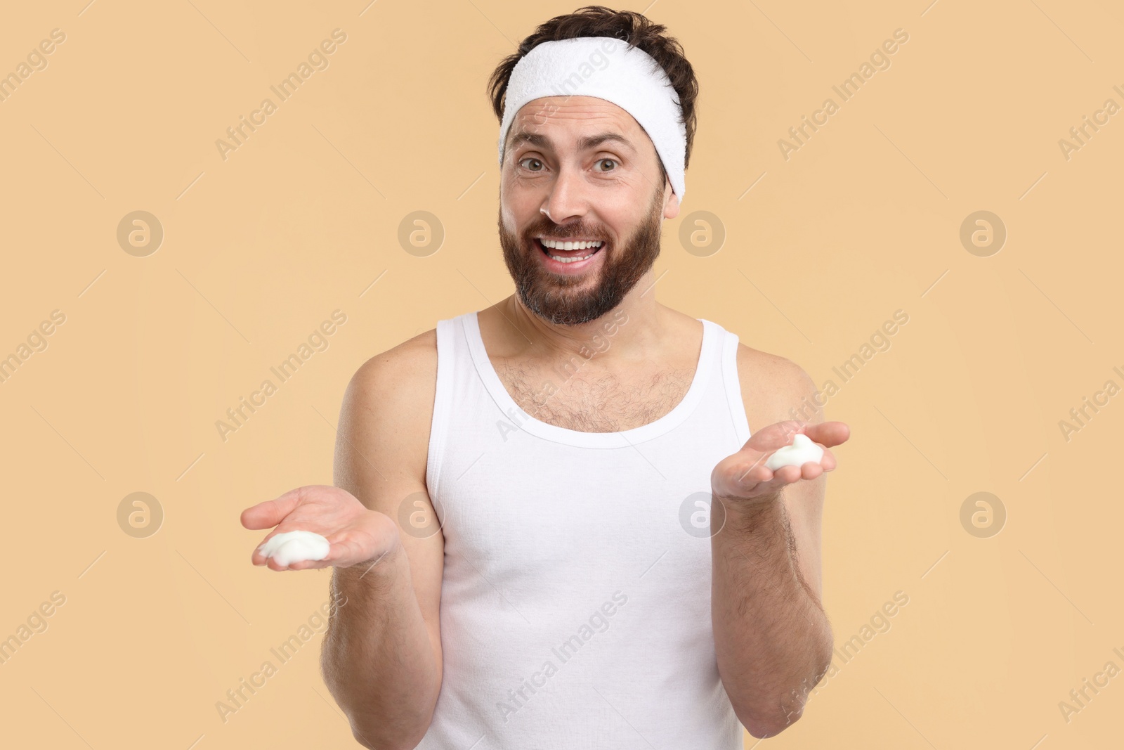 Photo of Man with headband washing his face on beige background