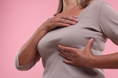 Woman doing breast self-examination on pink background, closeup