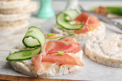 Puffed rice cakes with prosciutto and cucumber on wooden board, closeup