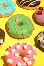 Different delicious glazed doughnuts on yellow background