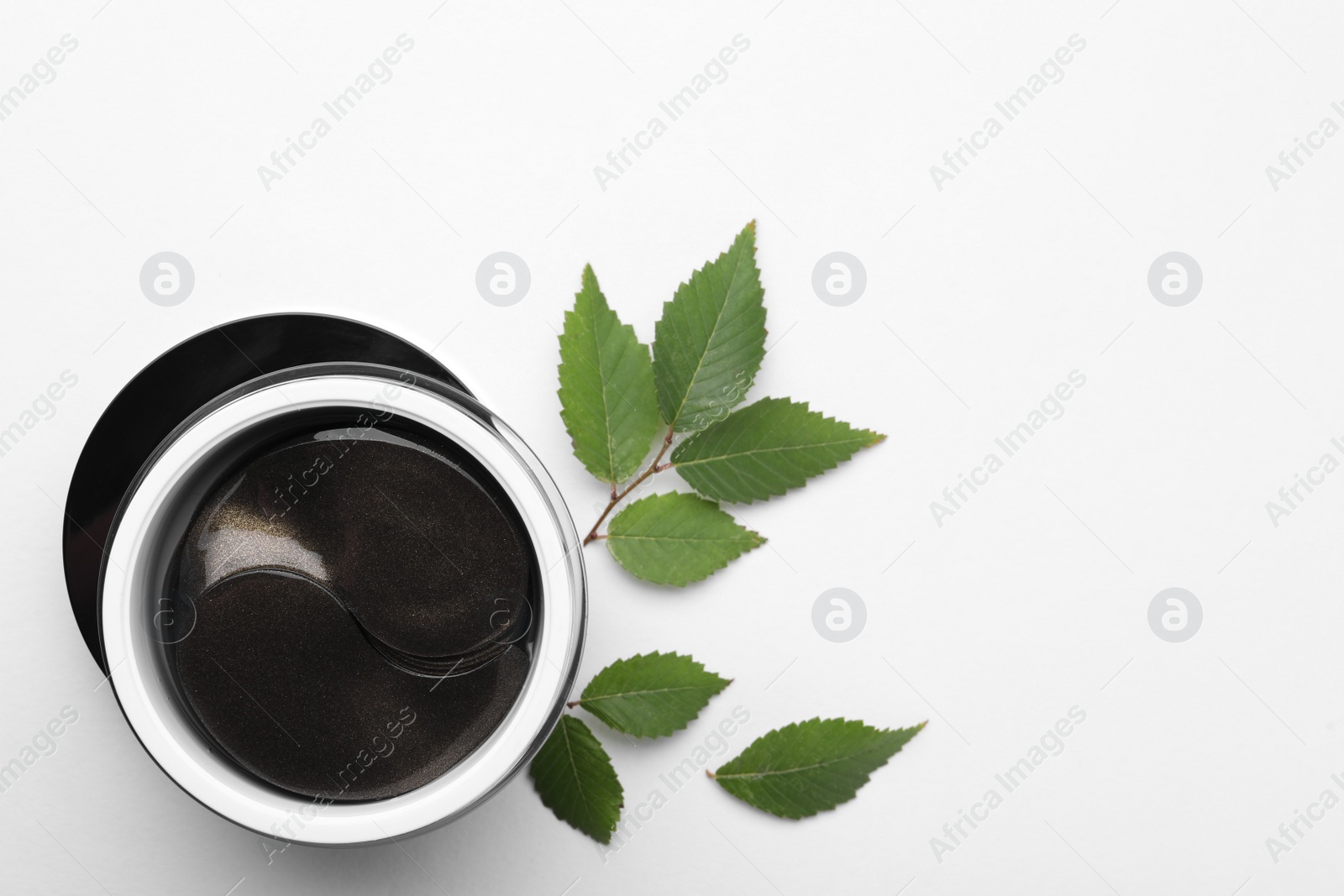 Photo of Under eye patches in jar near green leaves on white background, flat lay. Space for text