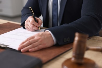 Photo of Notary writing notes at wooden table in office, closeup