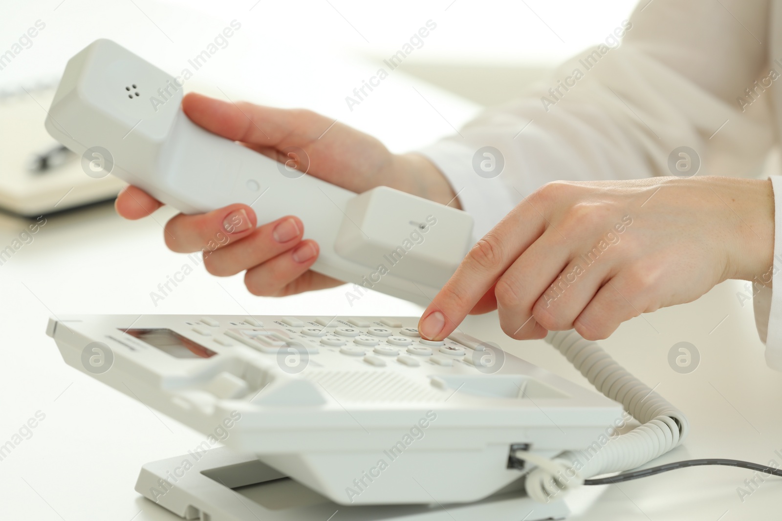 Photo of Assistant dialing number on telephone at white table, closeup