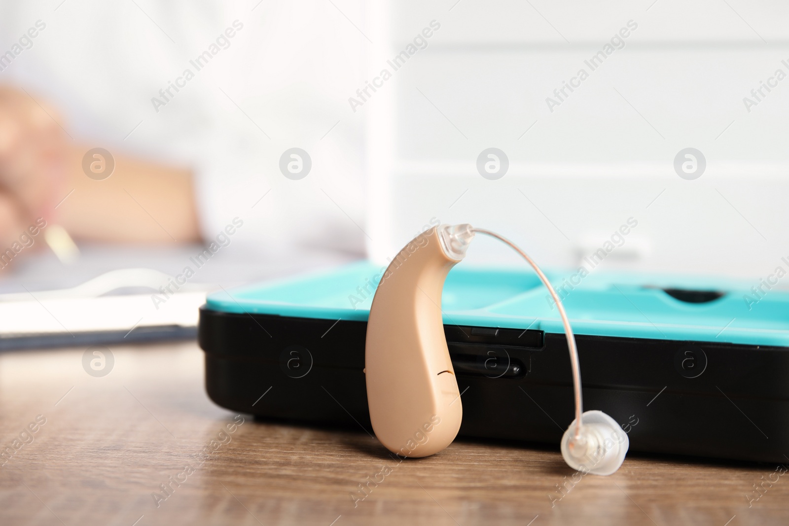 Photo of Hearing aid with box on wooden table. Medical device