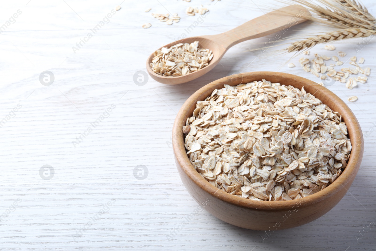 Photo of Oatmeal, bowl and spoon on white wooden table. Space for text