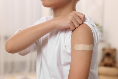 Photo of Boy with sticking plaster on arm after vaccination indoors, closeup