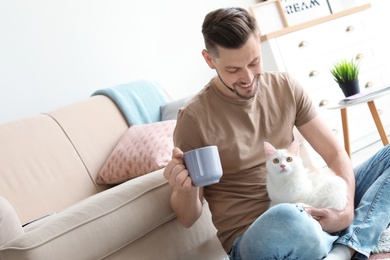 Photo of Young man with cute cat sitting on floor at home