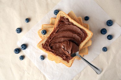 Photo of Tasty toast with chocolate paste and blueberries on parchment paper, flat lay