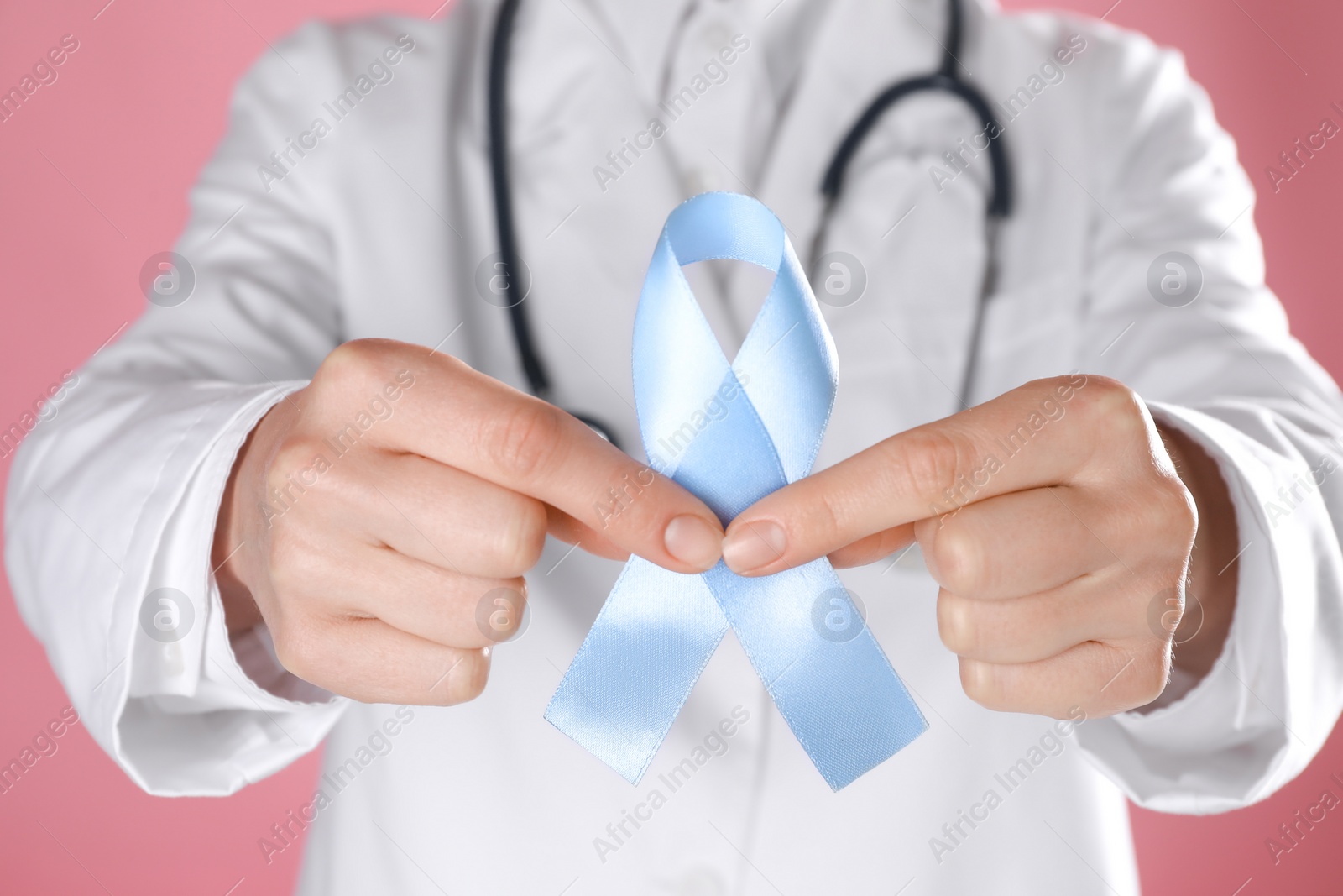 Photo of International Psoriasis Day. Doctor with light blue ribbon as symbol of support on pink background, closeup