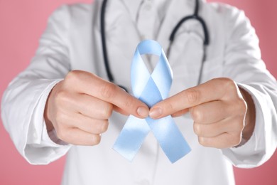 International Psoriasis Day. Doctor with light blue ribbon as symbol of support on pink background, closeup