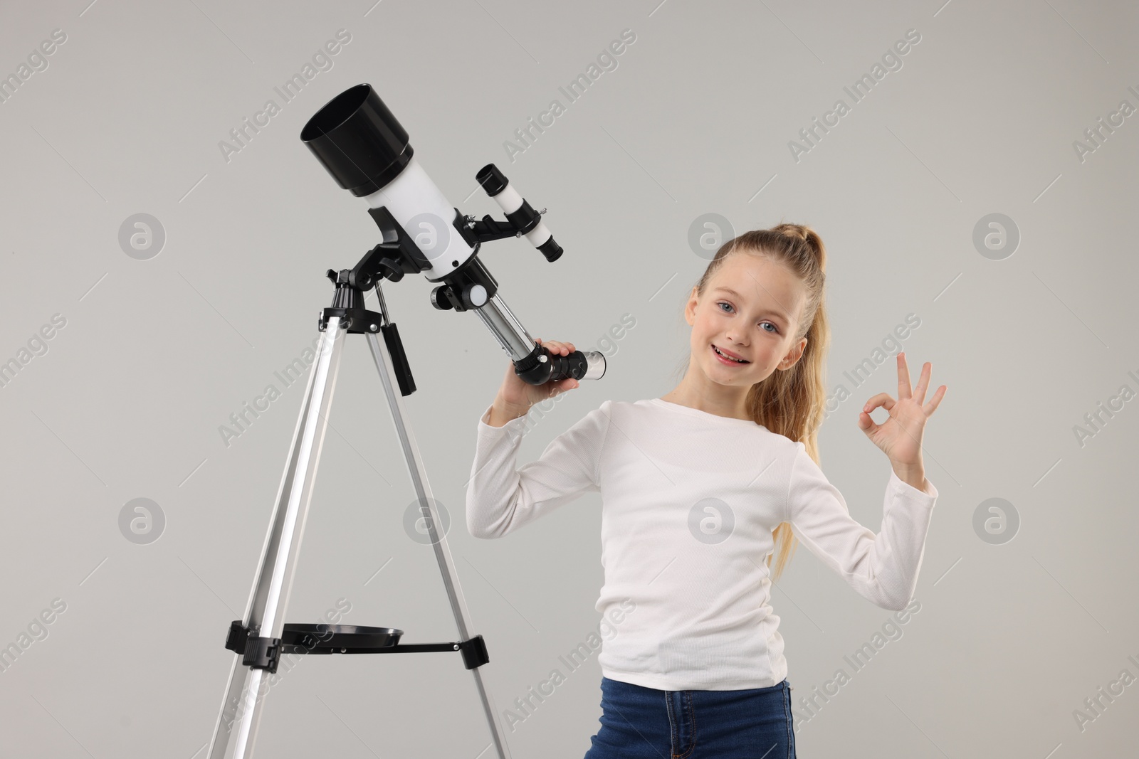 Photo of Happy little girl with telescope showing ok gesture on light grey background