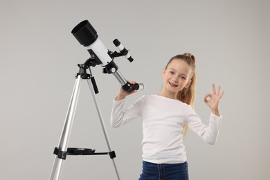 Happy little girl with telescope showing ok gesture on light grey background