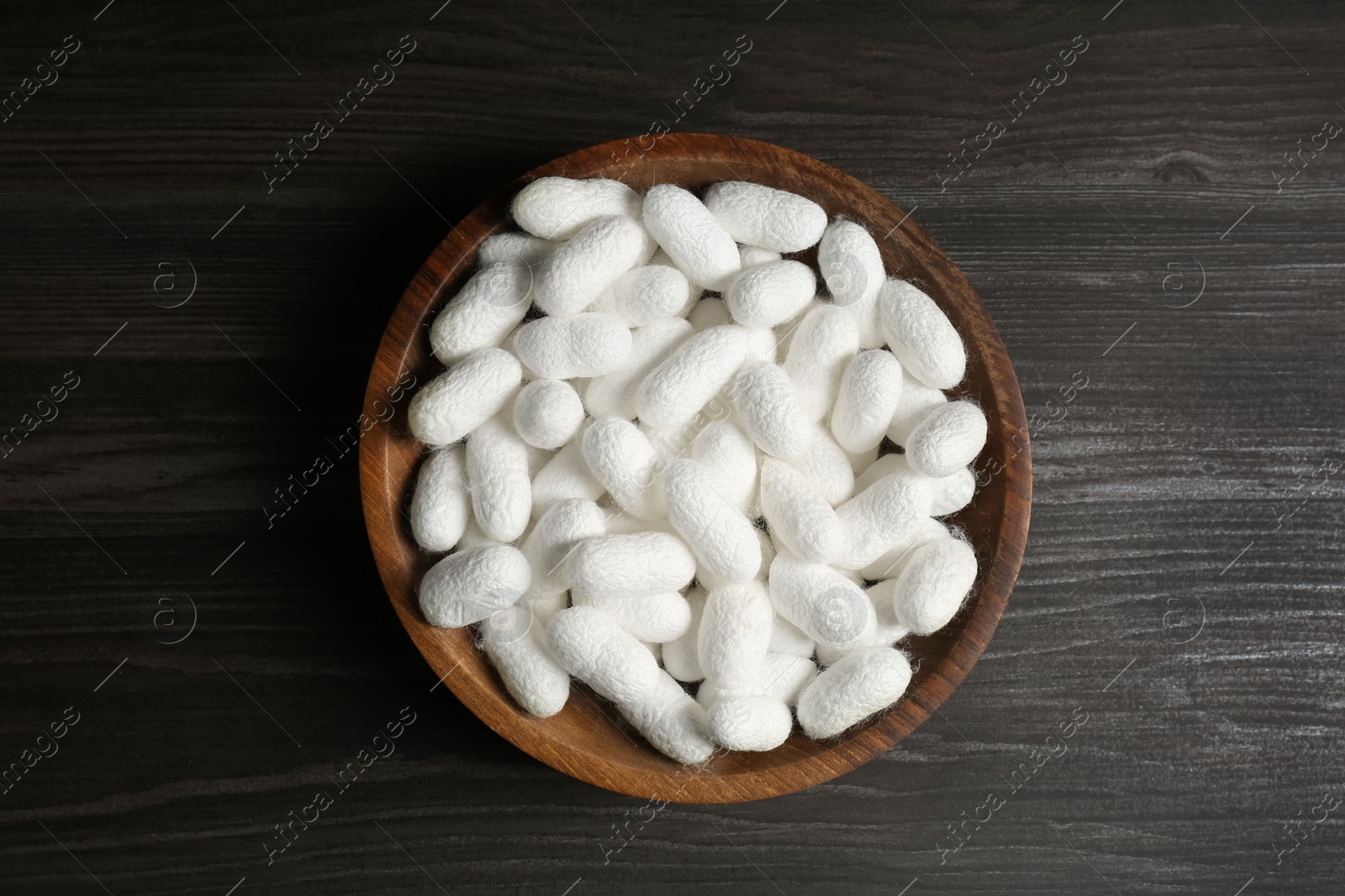 Photo of White silk cocoons in bowl on wooden table, top view