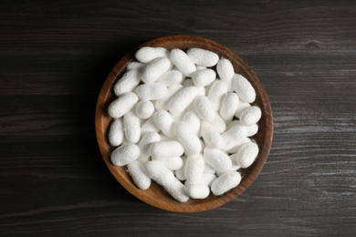 Photo of White silk cocoons in bowl on wooden table, top view