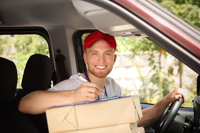 Young courier with parcels and clipboard in delivery car