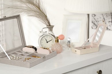 Jewelry boxes with many different accessories, perfumes, alarm clock and decor on white wooden table indoors