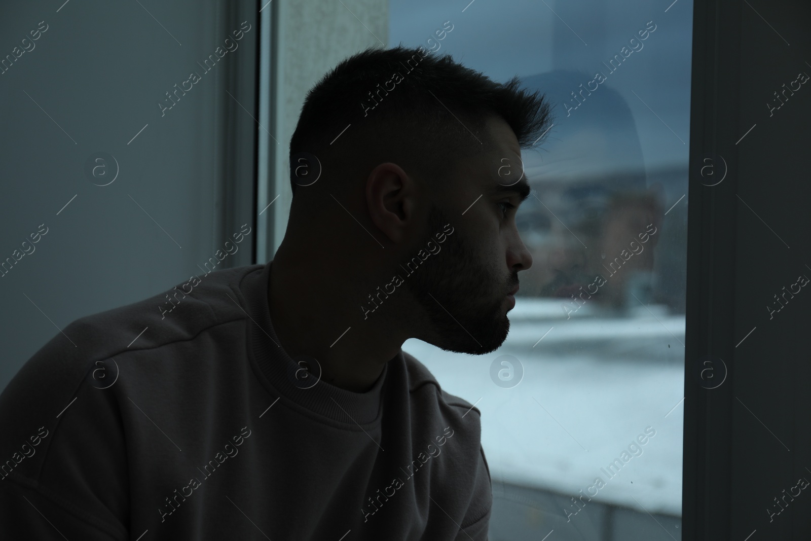 Photo of Sad man looking at window in dark room