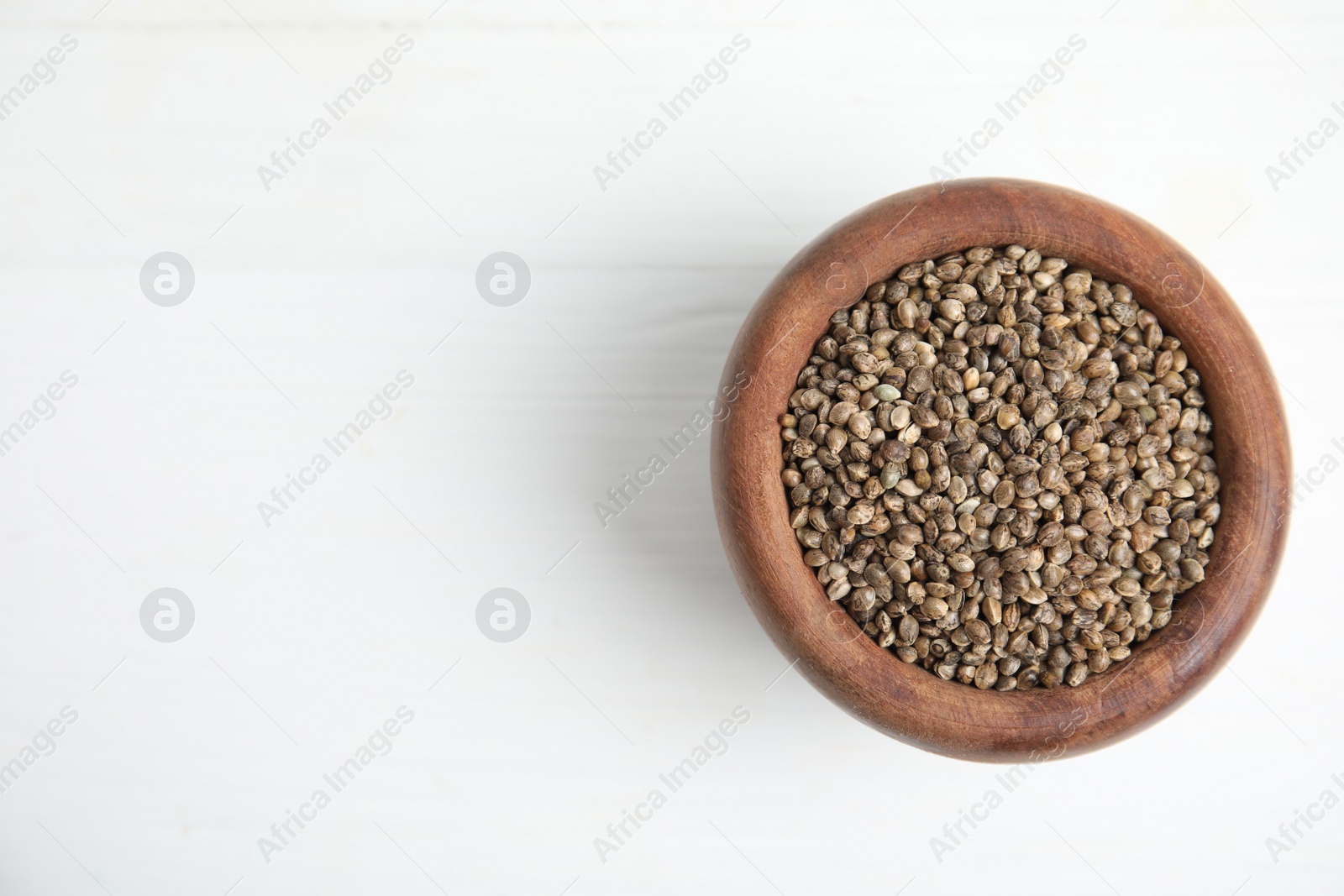 Photo of Wooden bowl with organic hemp seeds on white table, top view. Space for text