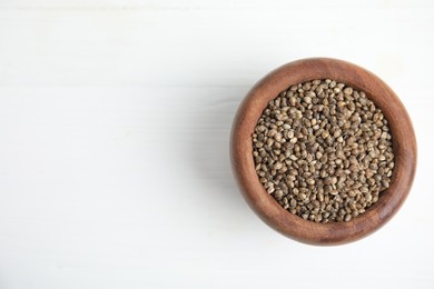 Wooden bowl with organic hemp seeds on white table, top view. Space for text