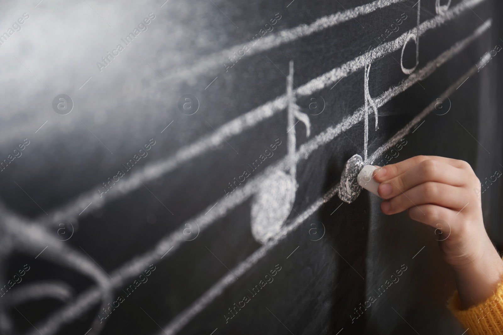Photo of Child writing music notes on blackboard, closeup