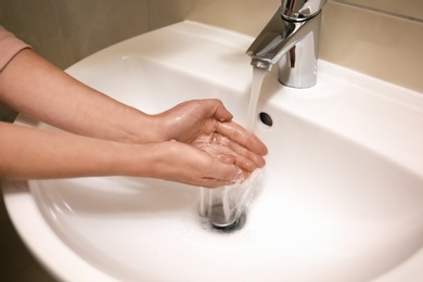 Woman washing hands with soap under running water in bathroom