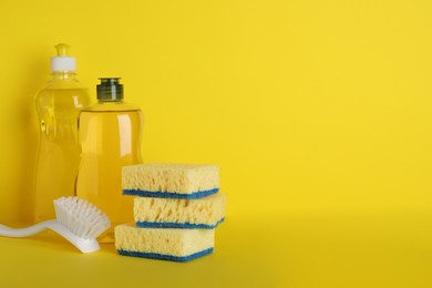 Photo of Sponges and other cleaning products on yellow background. Space for text