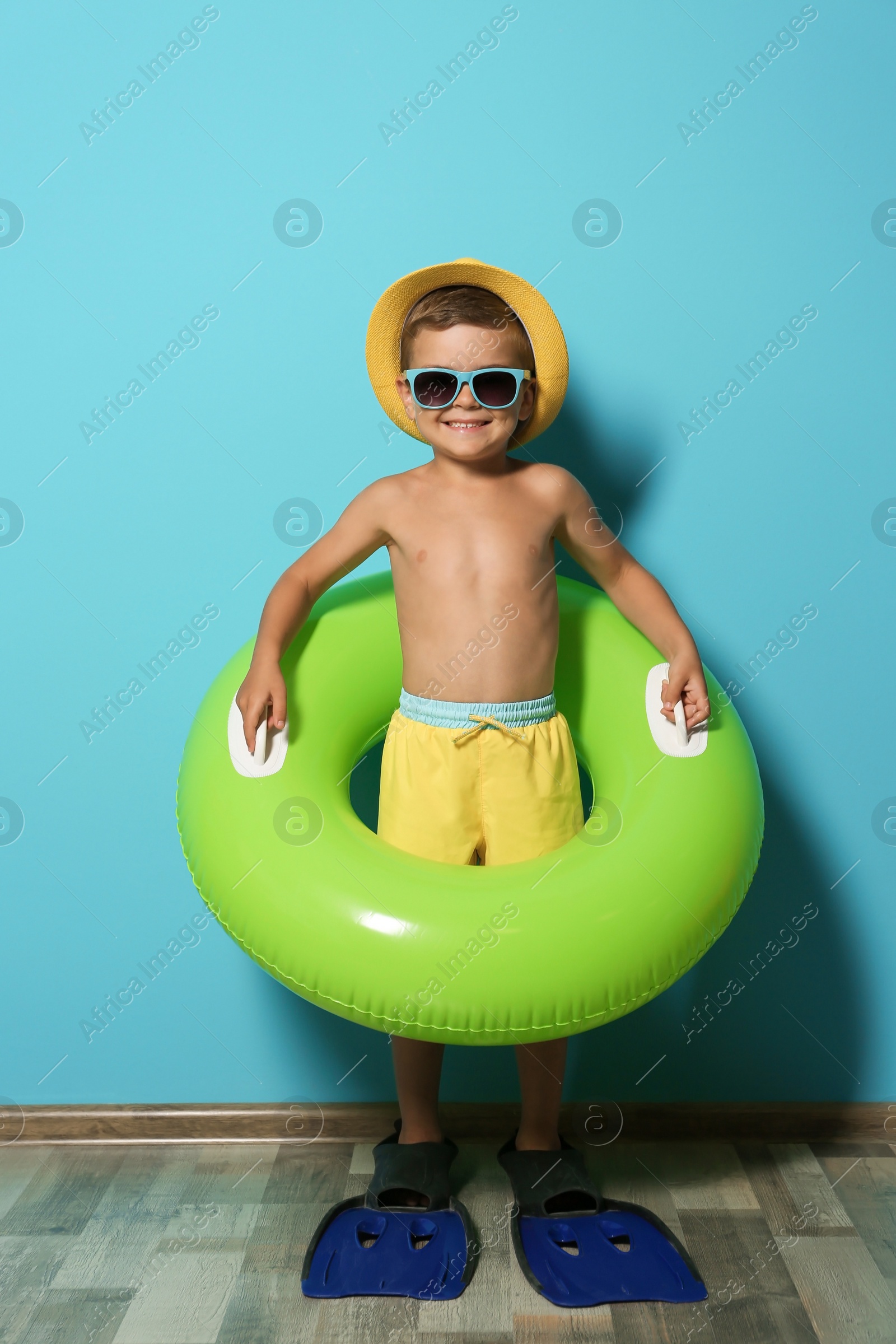 Photo of Cute little boy with inflatable ring wearing flippers near color wall