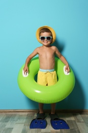 Cute little boy with inflatable ring wearing flippers near color wall