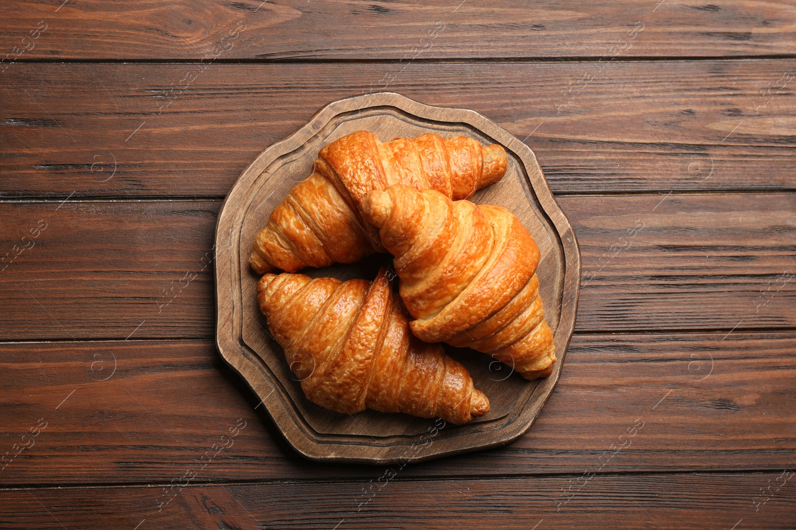 Photo of Board with tasty croissants on wooden background, top view. French pastry