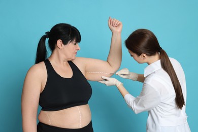 Photo of Doctor with scalpel near obese woman on light blue background. Weight loss surgery