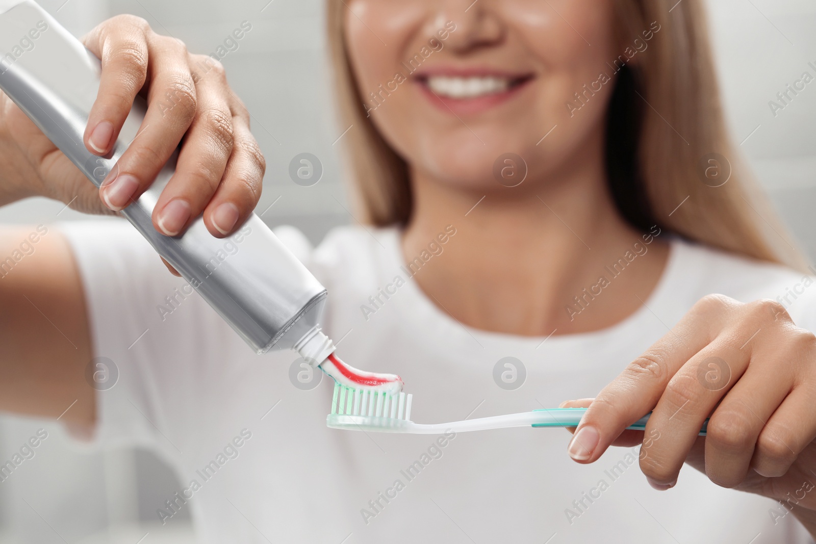 Photo of Woman applying toothpaste on brush in bathroom, closeup