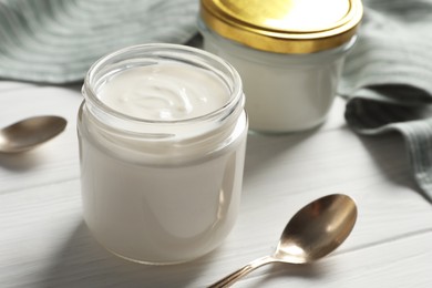 Photo of Jars with delicious organic yogurt on white wooden table, closeup