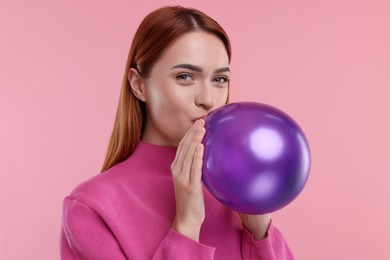 Photo of Woman inflating purple balloon on pink background