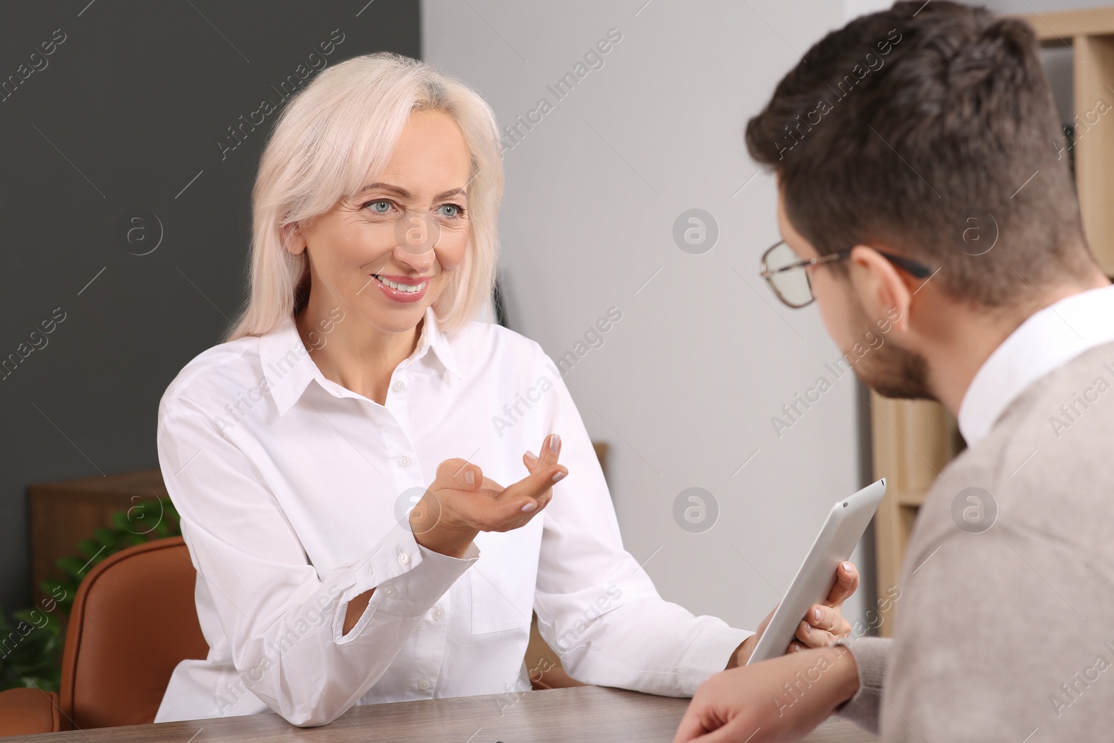 Photo of Happy woman having conversation with man at wooden table in office. Manager conducting job interview with applicant