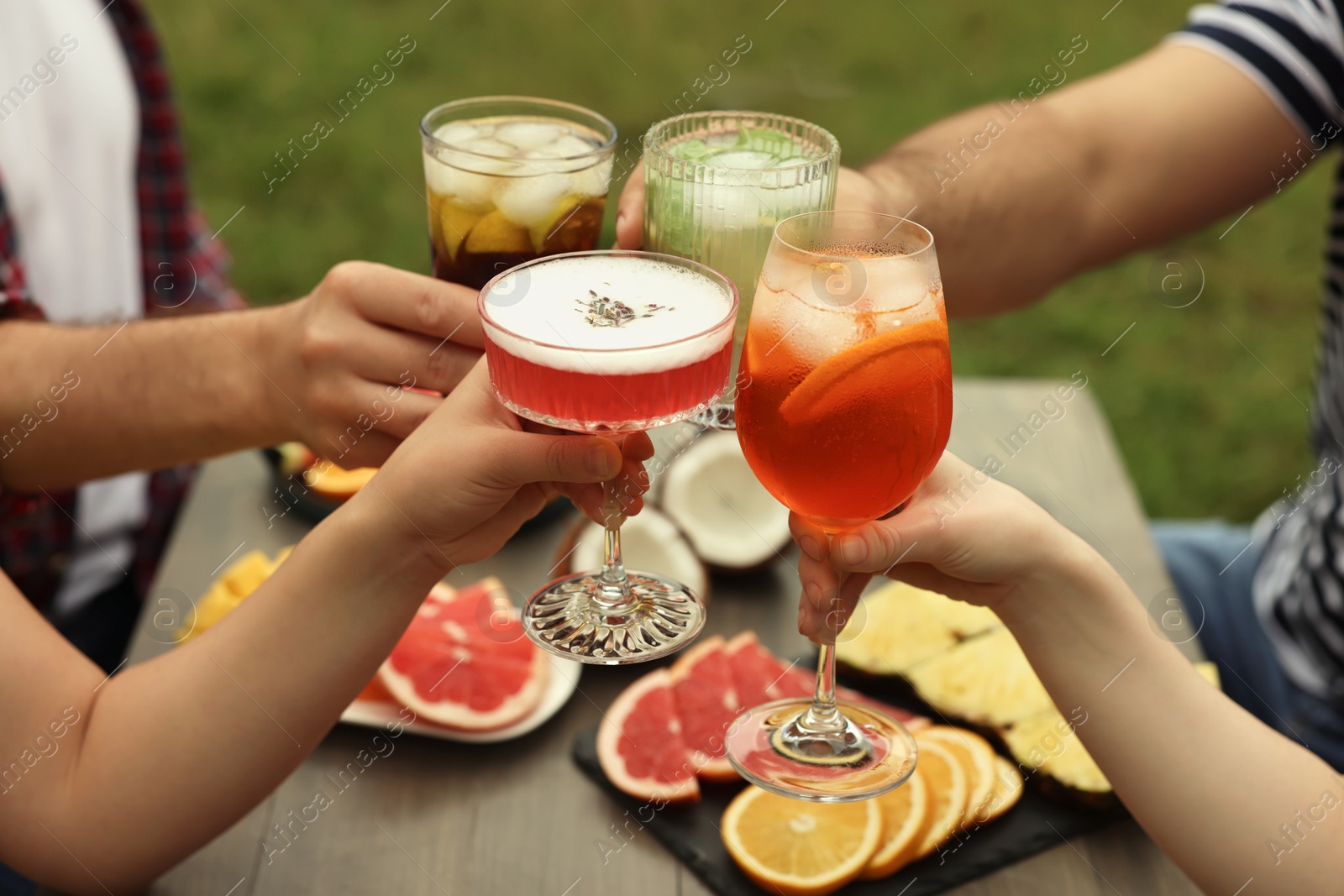 Photo of Friends clinking glasses with cocktails at table outdoors, closeup