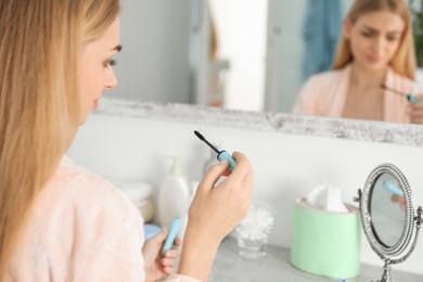 Young woman holding mascara brush with fallen eyelashes indoors