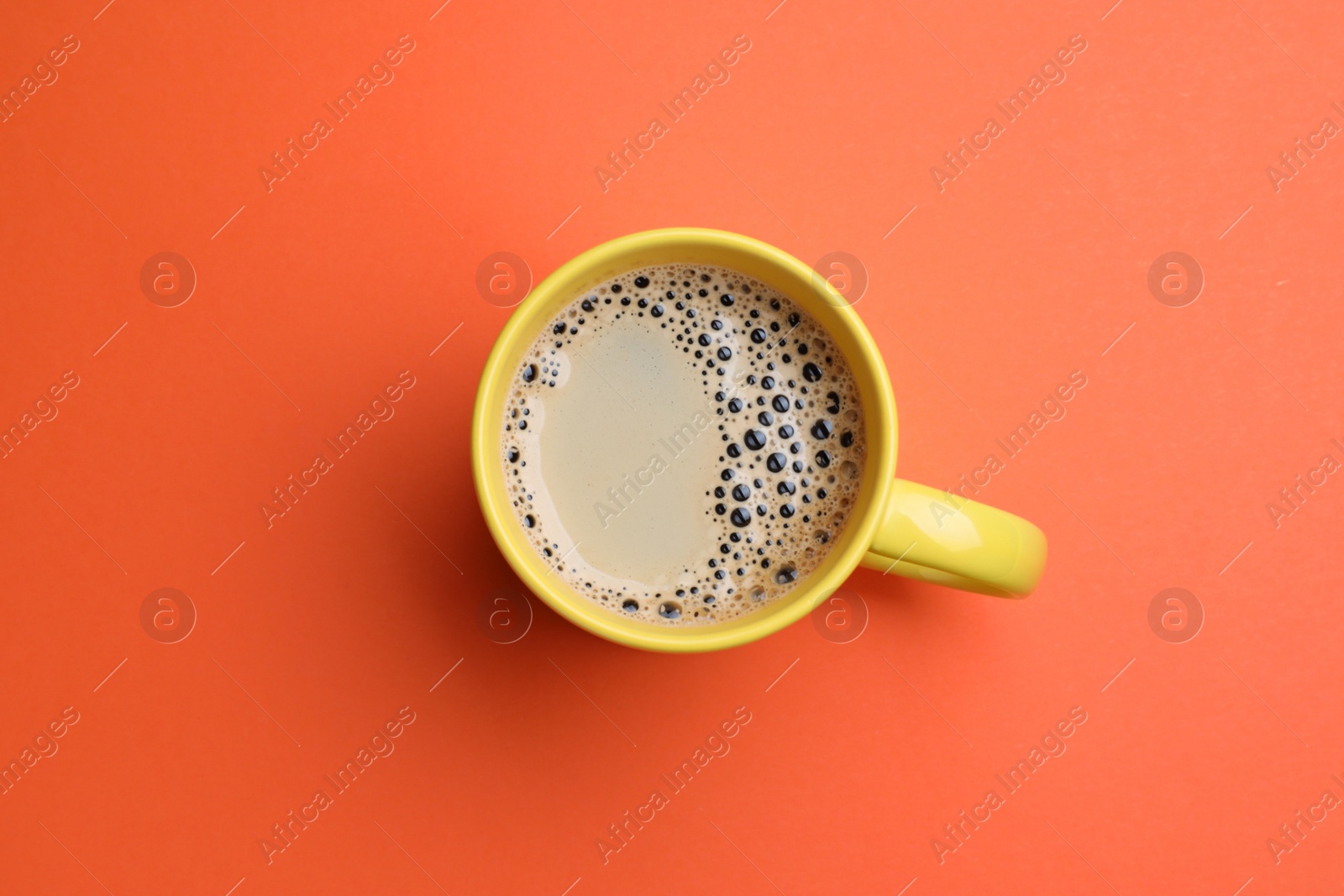 Photo of Yellow mug of freshly brewed hot coffee on orange background, top view