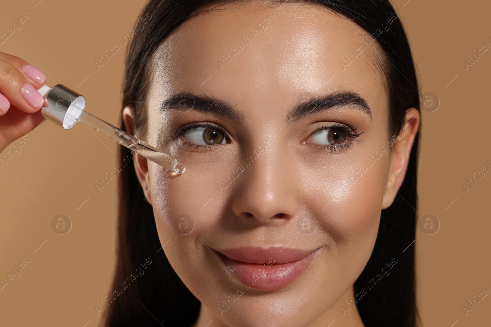 Photo of Beautiful young woman applying serum onto her face on beige background, closeup