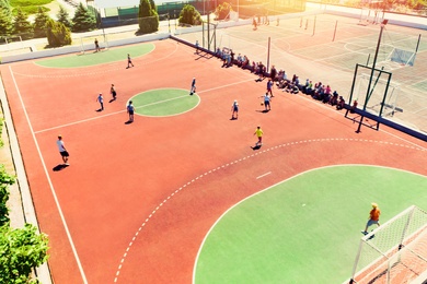 Image of Children playing soccer at outdoor sports complex on sunny day, aerial view