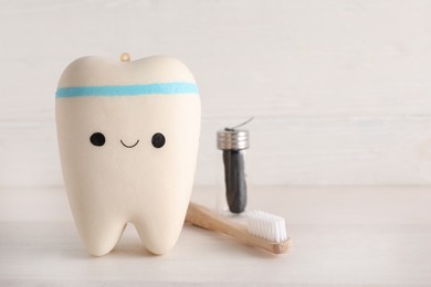 Photo of Tooth model with cute face, toothbrush and dental floss on white wooden table. Space for text