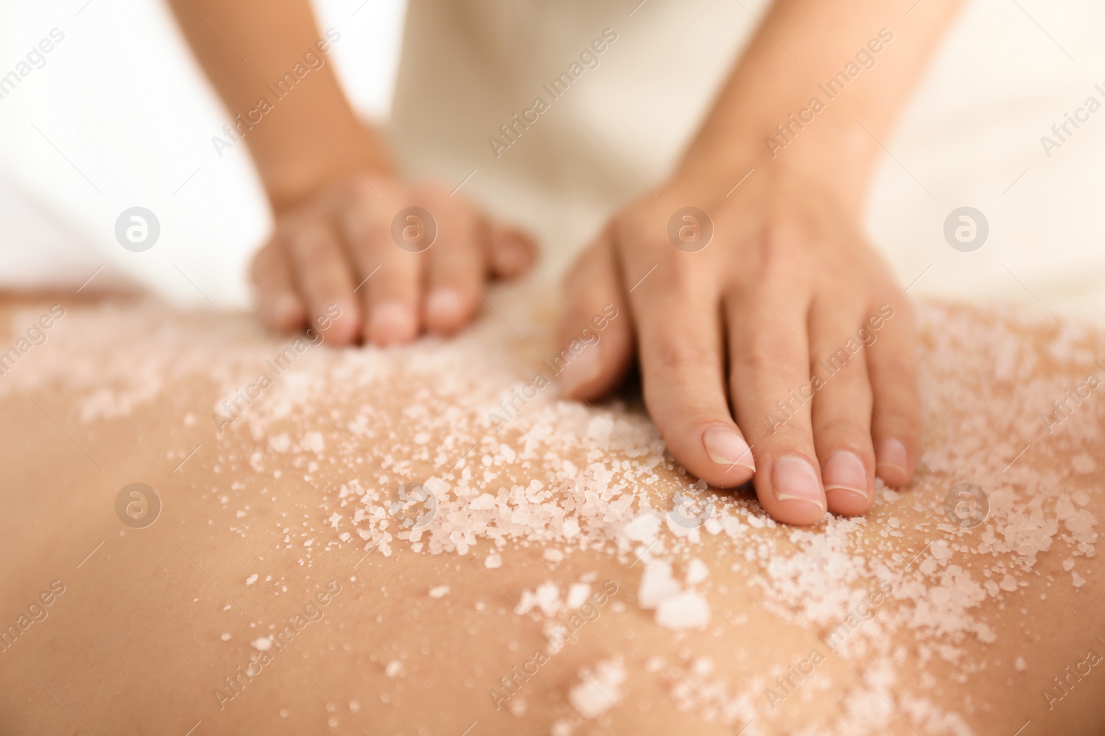 Photo of Young woman having body scrubbing procedure with sea salt in spa salon, closeup