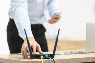 Photo of Man inserting cable into Wi-Fi router at wooden table indoors, closeup. Space for text