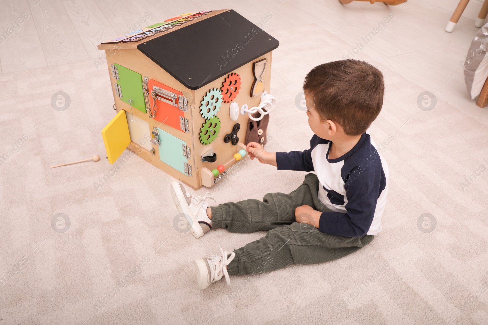 Photo of Little boy playing with busy board house on floor in room